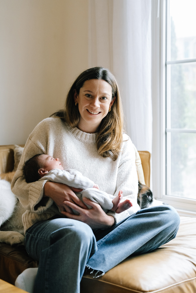 Mother sitting on couch holding newborn during lifestyle session