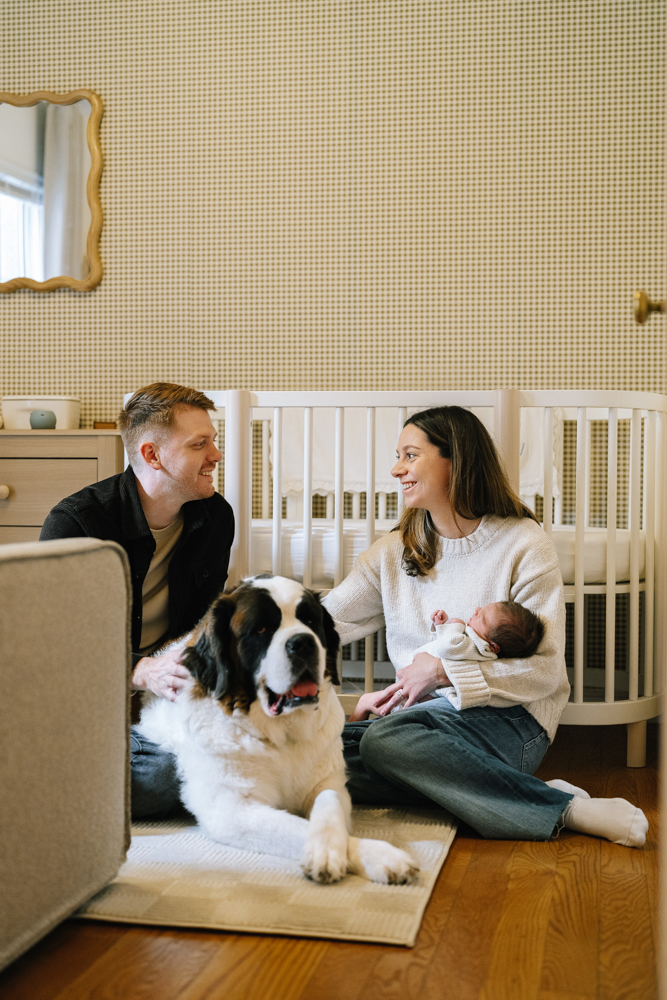 Parents sitting on nursery floor with baby and family dog