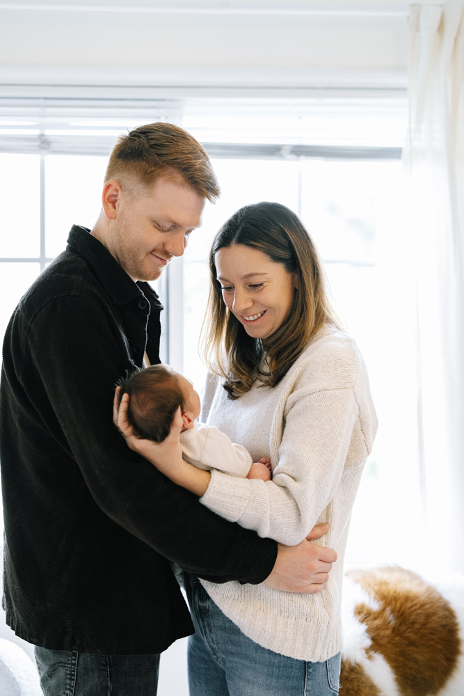Father holding newborn while mother stands beside him