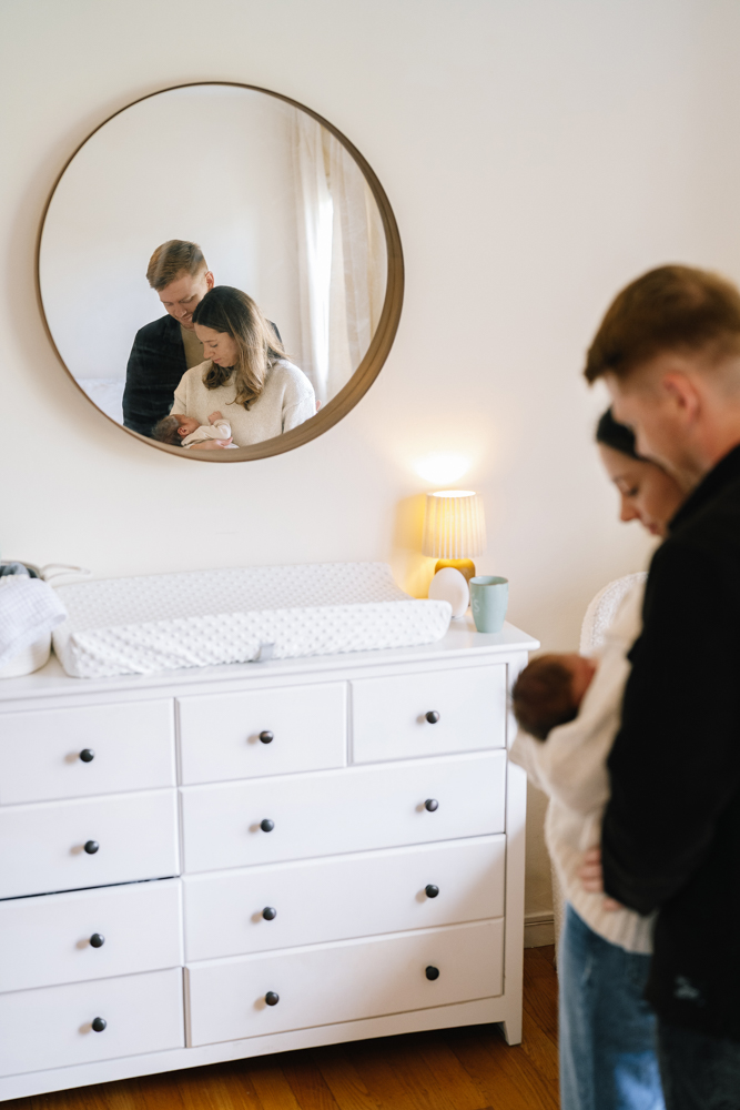 Father holding newborn near dresser and mirror