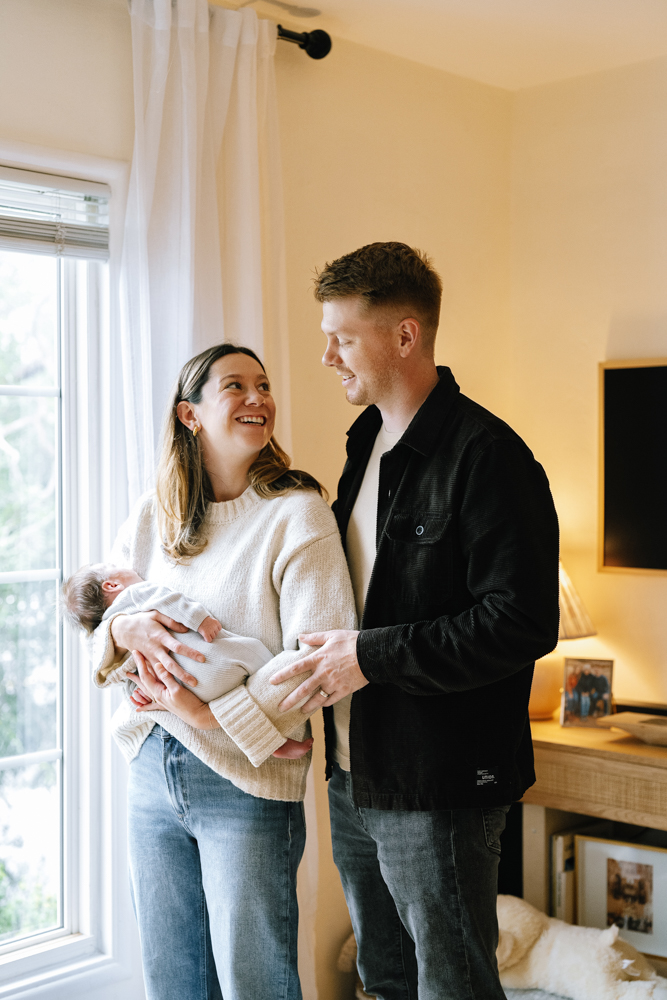 Parents standing together holding newborn in softly lit room