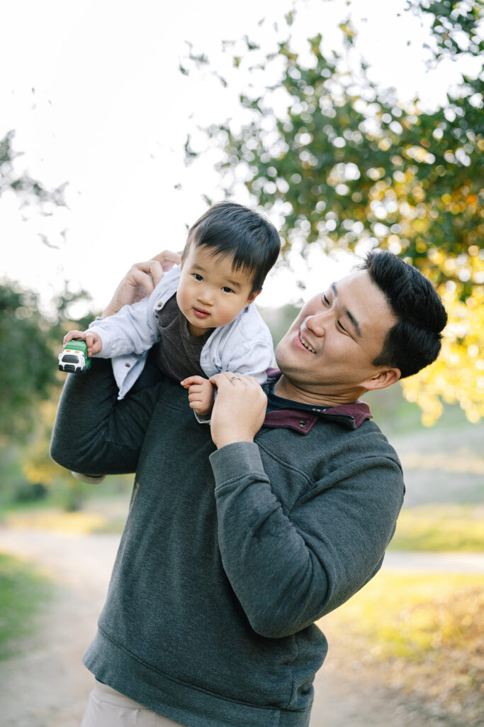 Candid family portrait Guadalupe Oak Grove Park San Jose — dad lifting toddler on shoulders on sunny park path