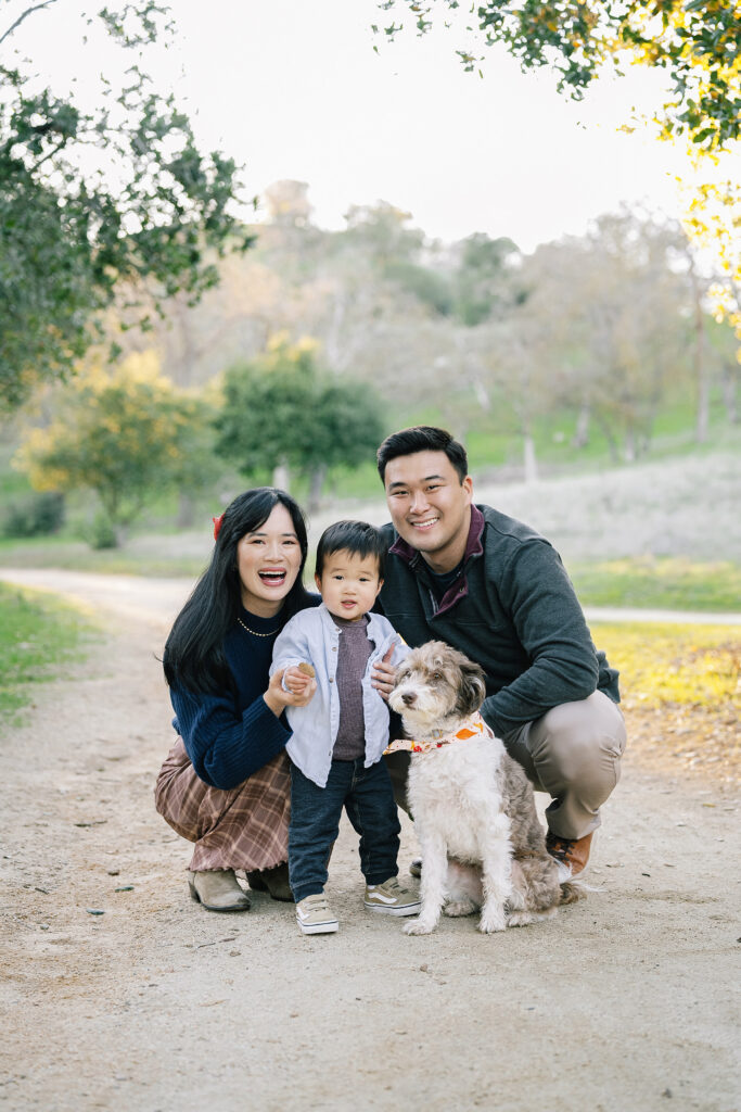 Lifestyle family session Guadalupe Oak Grove Park San Jose — family with toddler and dog on dirt path surrounded by oak trees