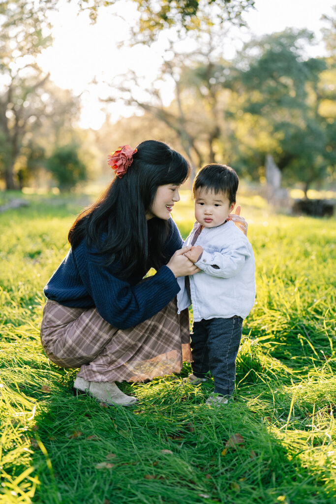 Family photography Guadalupe Oak Grove Park San Jose — mother crouching with toddler in green meadow at golden hour
