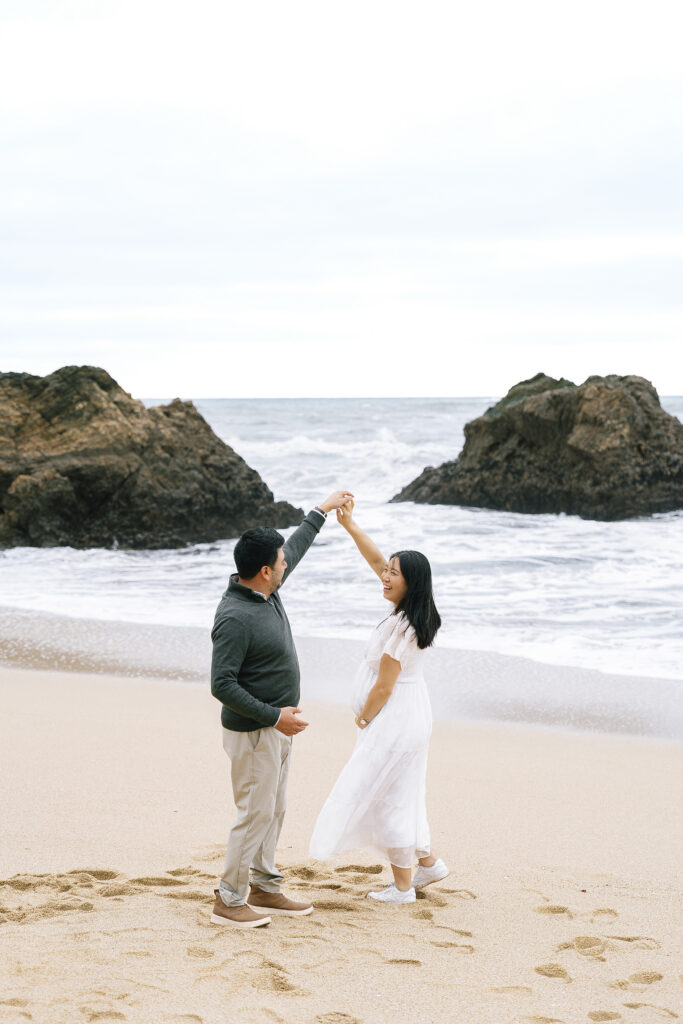 Maternity photographer Half Moon Bay — couple dancing on beach with dramatic rock formation