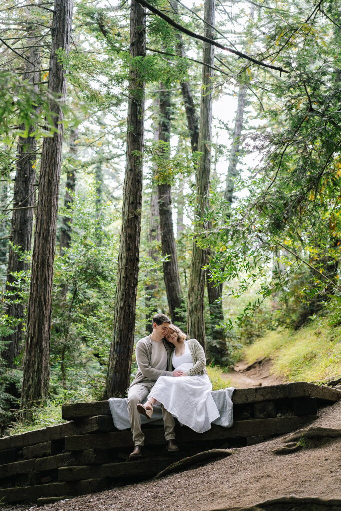 Maternity session Henry Cowell Redwoods State Park — couple sitting on log with towering redwood trees