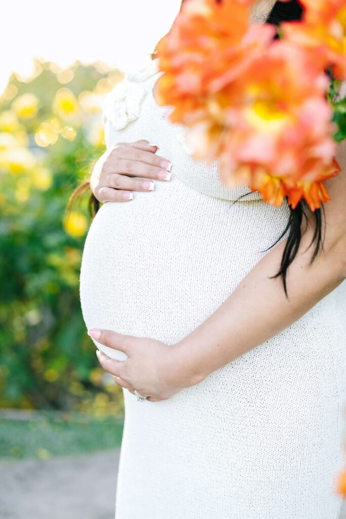 Close-up maternity portrait Municipal Rose Garden San Jose — baby bump with vibrant orange roses in foreground