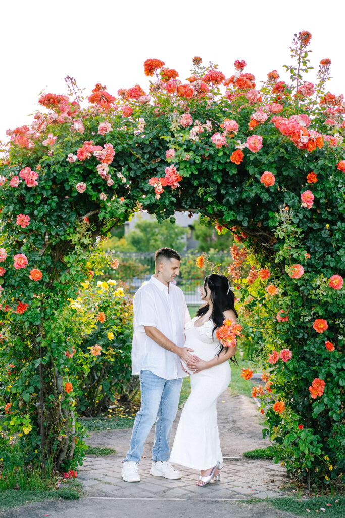 Maternity photography Municipal Rose Garden San Jose — couple standing under blooming rose arch Bay Area
