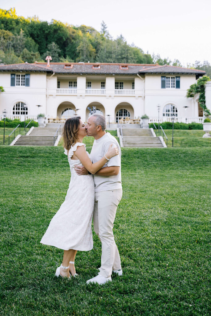 Family photographer Villa Montalvo Saratoga — couple kissing on lawn with Mediterranean villa in background