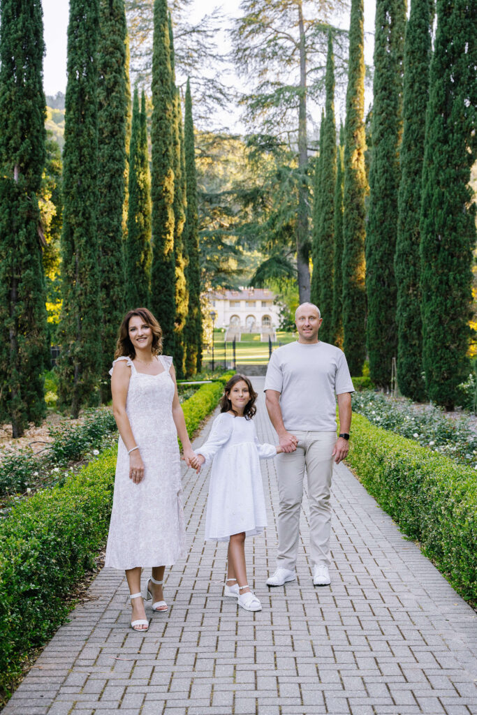 Lifestyle family session Villa Montalvo Saratoga — family of three walking along cypress tree alley Bay Area