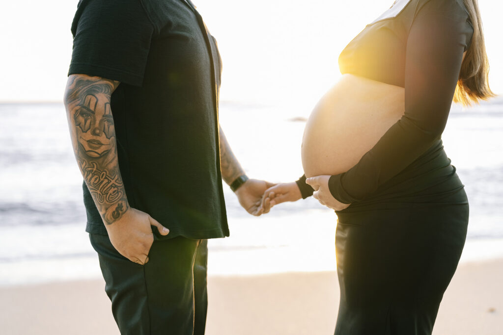 Maternity photo at Moss Beach California — couple holding hands at golden hour with baby bump
