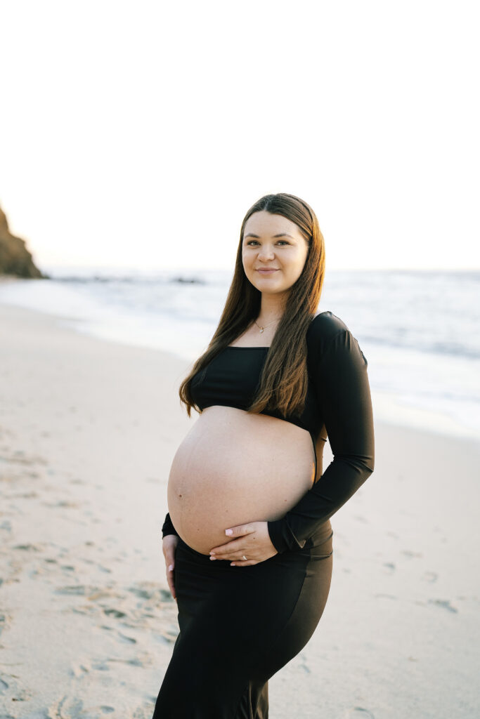 Maternity portrait at Moss Beach San Mateo County — woman in black top on sandy shore