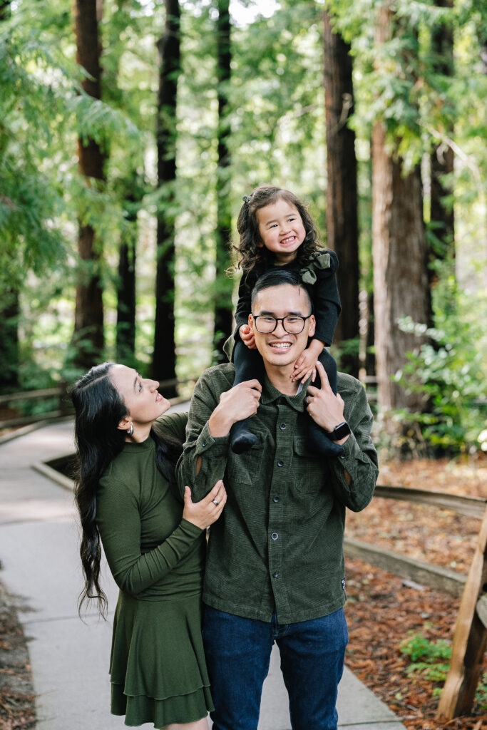 Family photographer Los Altos — dad with daughter on shoulders and mom on redwood grove nature preserve path