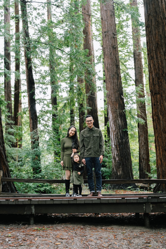 Lifestyle family session Redwood Grove Los Altos — family of three on wooden bridge surrounded by tall redwood trees