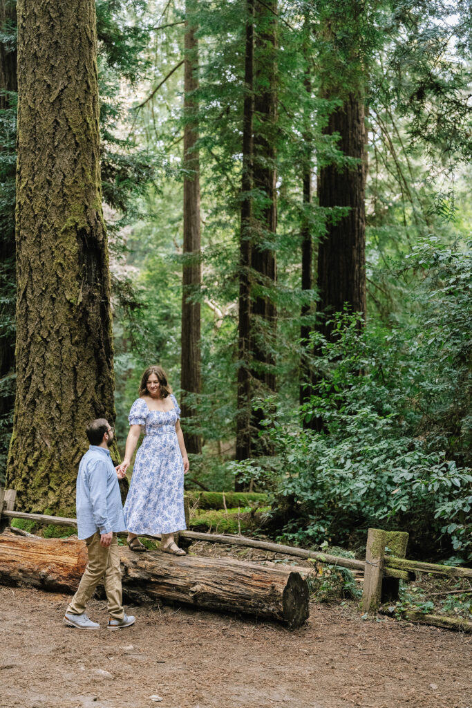 Maternity photography in Santa Cruz redwoods — couple standing on fallen log surrounded by tall trees